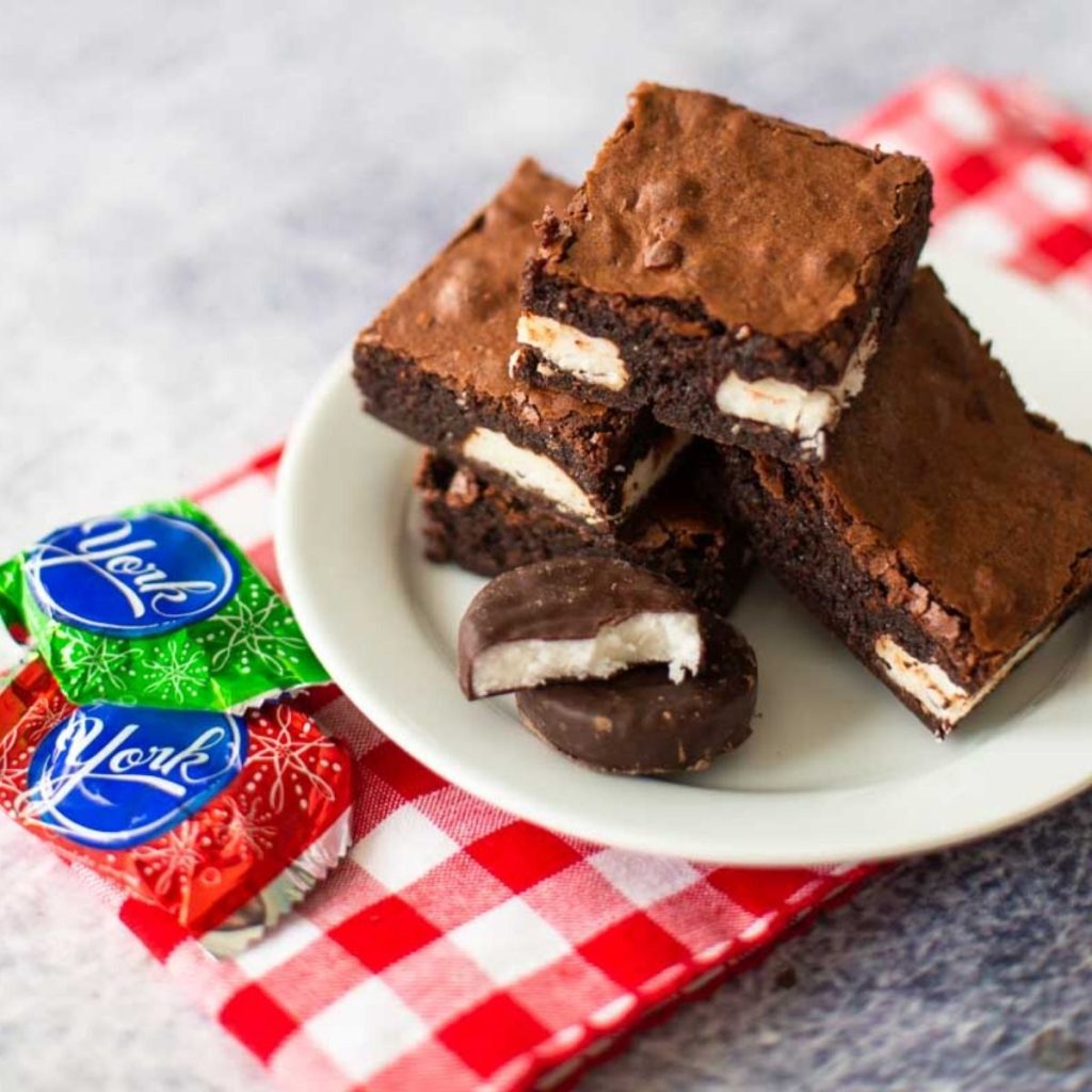 A white plate has a pile of brownies on it. Each brownie has a layer of peppermint patty candy inside.