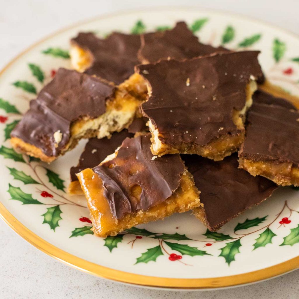 A holiday plate has chocolate coated cracker toffee in a pile.
