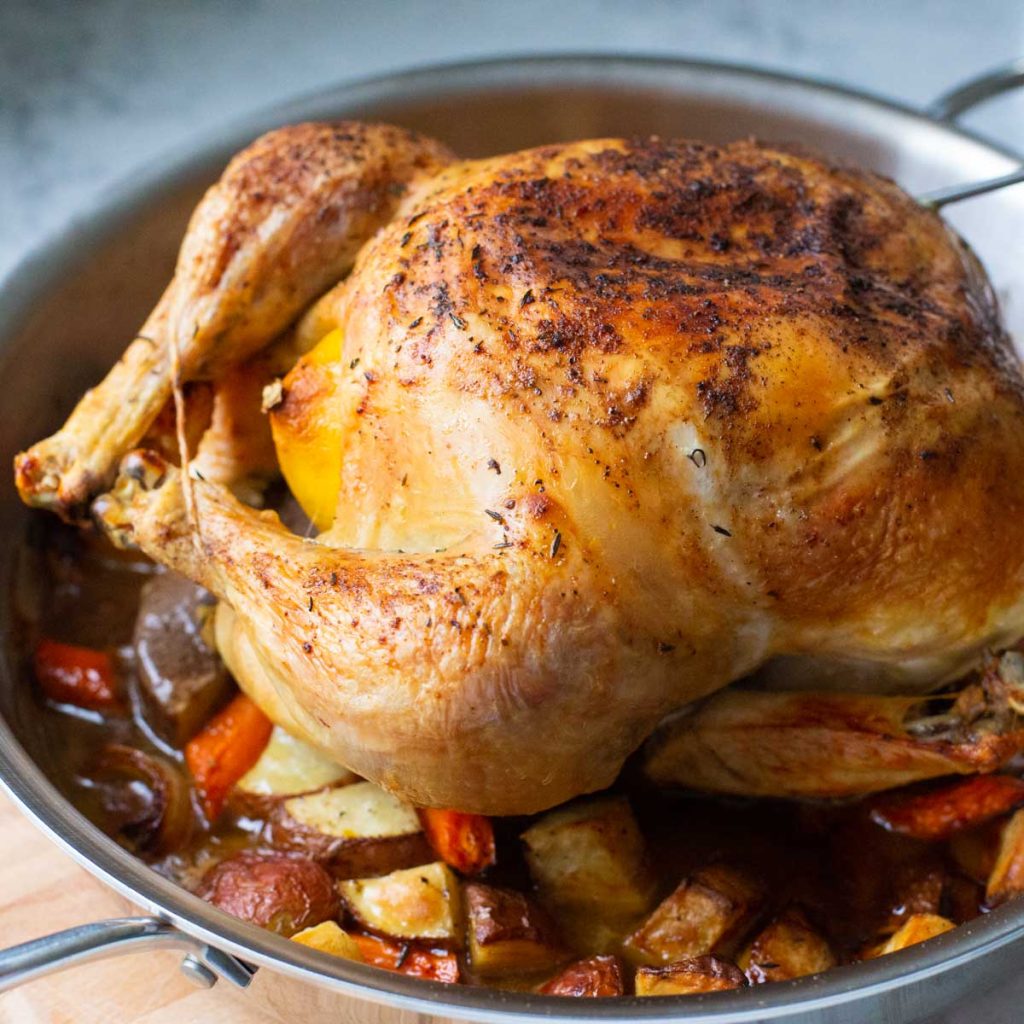 A roast chicken on a bed of vegetables in a skillet.