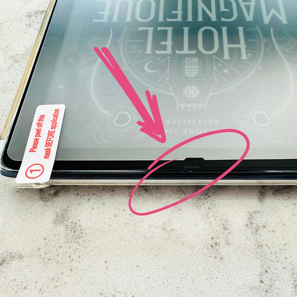 The image shows a close-up of the little notch on one side of the Kindle screen where you should line up the protector.