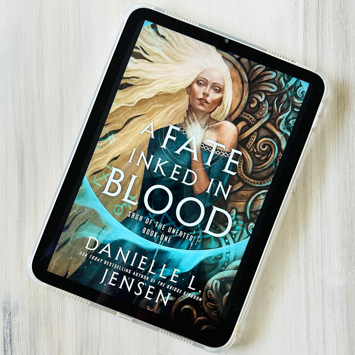 The cover of the book A Fate Inked in Blood by Danielle L. Jensen is on the screen of an iPad.