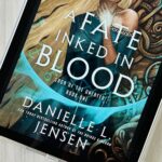 The cover of the book A Fate Inked in Blood by Danielle L. Jensen is on an iPad screen.