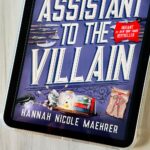 The cover of the book Assistant to the Villain by Hannah Nicole Maehrer is on the screen of an ipad.