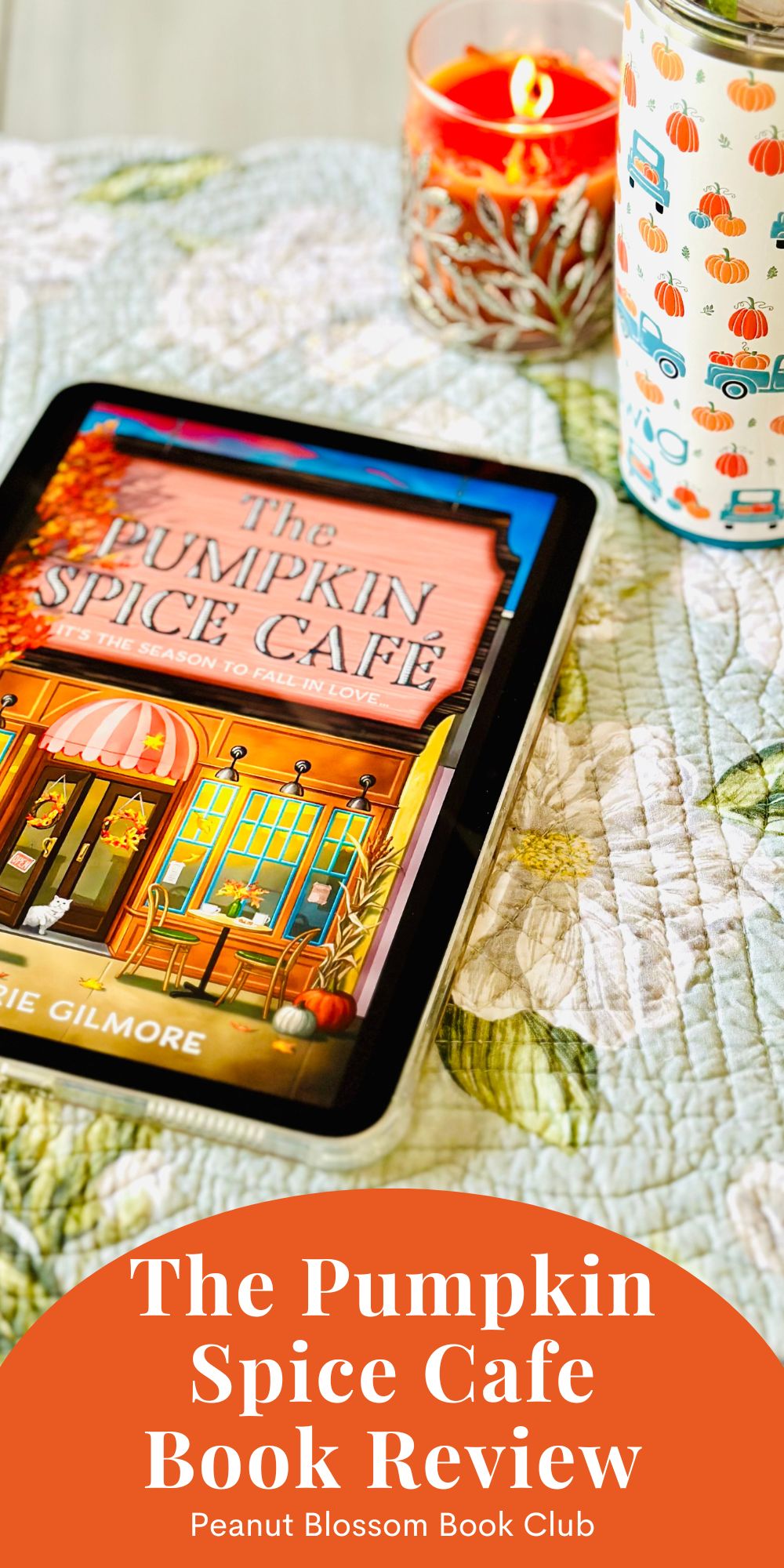 The cover of the book The Pumpkin Spice Cafe by Laurie Gilmore is on the screen of an iPad sitting next to a pumpkin coffee mug and an orange candle.