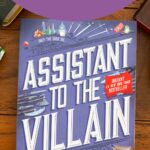 A copy of the book Assistant to the Villain by Hannah Nicole Maehrer sits on the table.