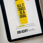 The cover of All It Takes is a Goal by Jon Acuff is on the screen of an ipad.