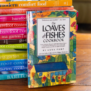 A copy of The Loaves and Fishes Cookbook by Anna Pump rests against a stack of Barefoot Contessa cookbooks.