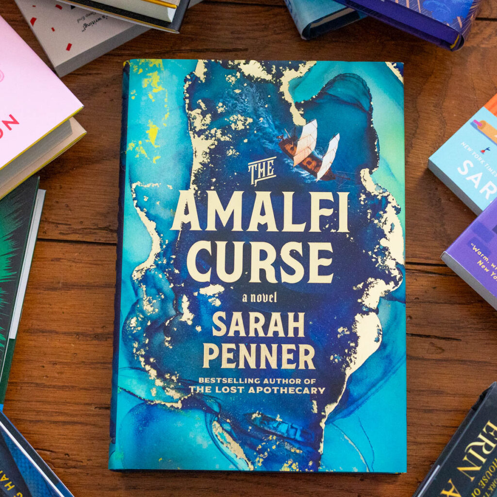 A copy of The Amalfi Curse by Sarah Penner sits on the table.