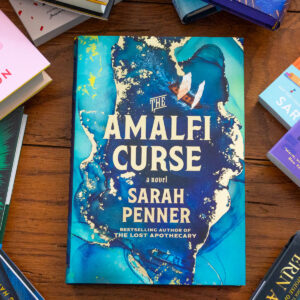 A copy of The Amalfi Curse by Sarah Penner sits on the table.