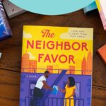 A copy of The Neighbor Favor by Kristina Forest sits on the table.