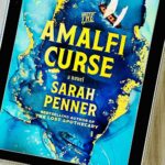 The cover of the book The Amalfi Curse by Sarah Penner is on the screen of an iPad.