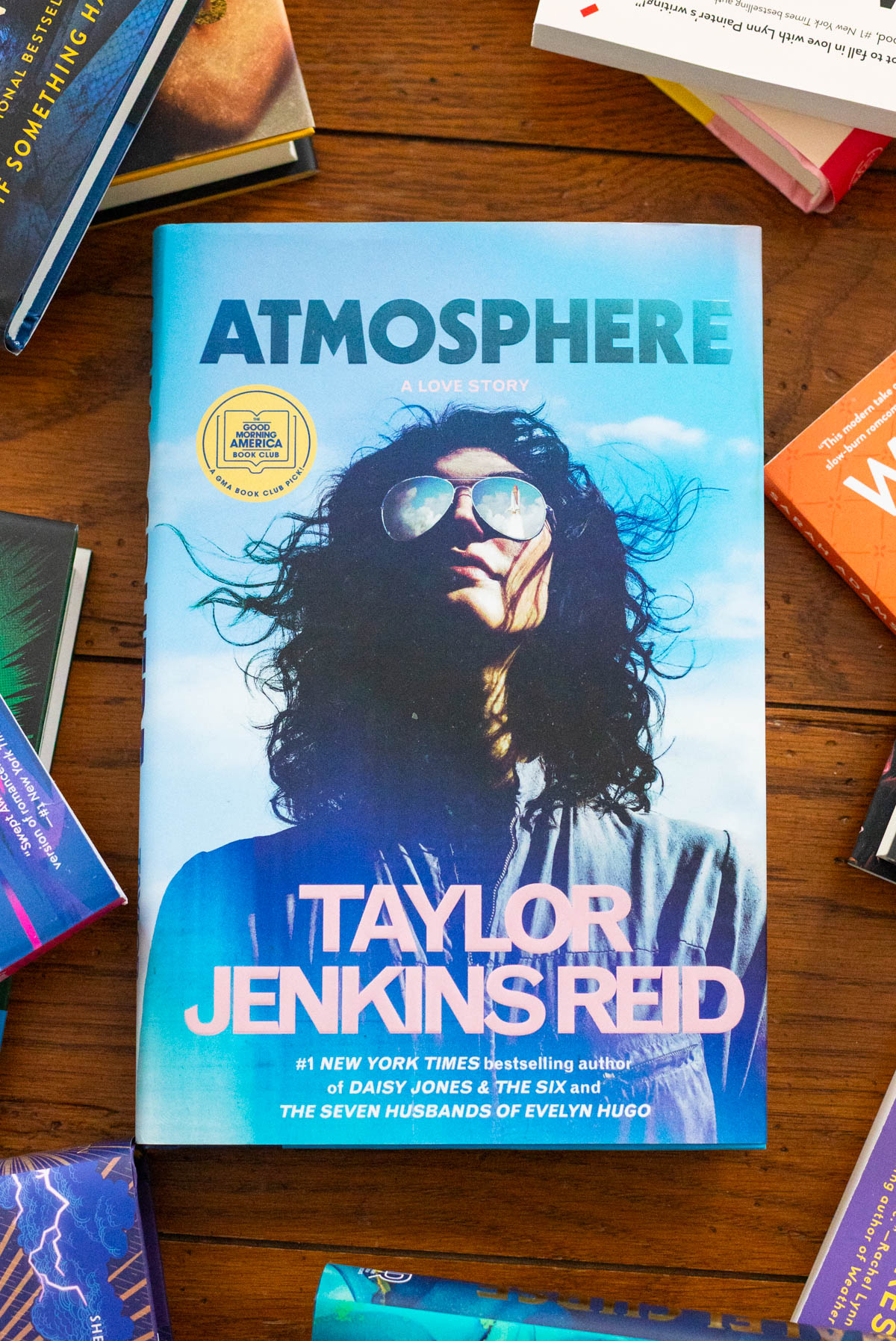 A copy of the book Atmosphere by Taylor Jenkins Reid sits on a table surrounded by more books.