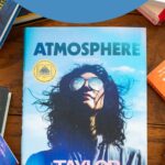 A copy of the book Atmosphere by Taylor Jenkins Reid sits on a table surrounded by more books.