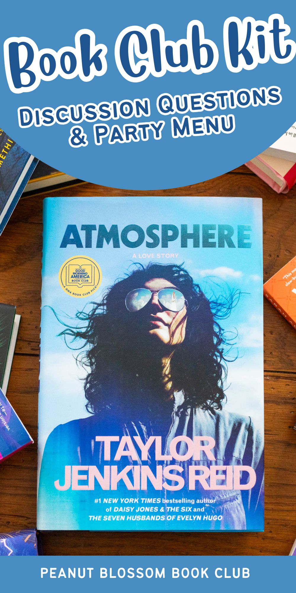 A copy of the book Atmosphere by Taylor Jenkins Reid sits on a table surrounded by more books.