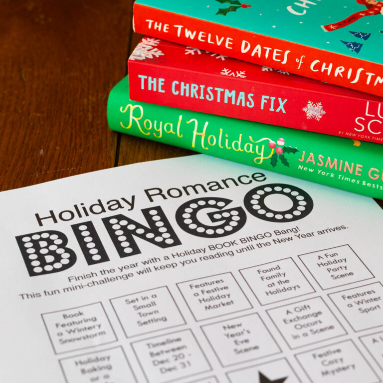 A Christmas reading challenge BINGO card sits on the table in front of a stack of holiday books.