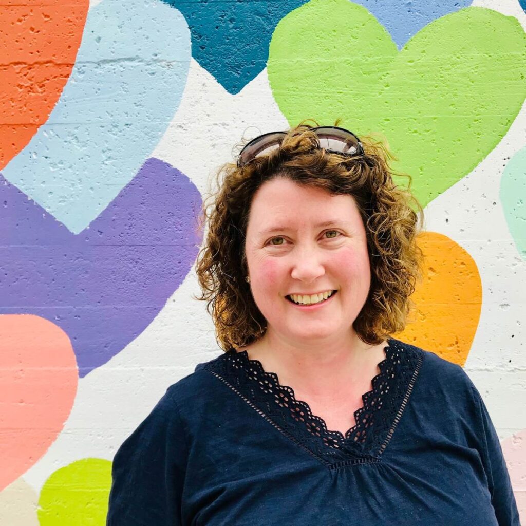 A picture of Tiffany Dahle standing against a mural painted with hearts.